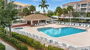 A pool area with lounge chairs and a covered seating area, surrounded by palm trees and a fence.