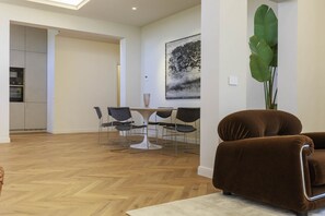 A modern living room with a brown sofa, a dining area with a white table and black chairs, and a large green plant.