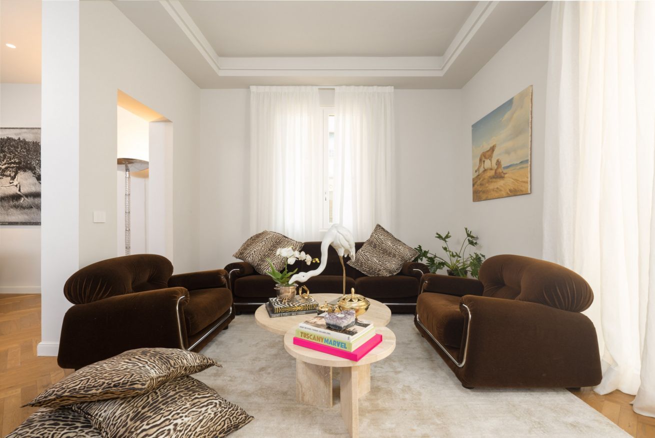 Un soggiorno con due divani marroni, un tavolino da caffè con libri e oggetti decorativi, un'orchidea bianca e un quadro appeso al muro.