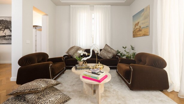 Un salón con dos sofás marrones, una mesa de centro con libros y objetos decorativos, una orquídea blanca y un cuadro en la pared.
