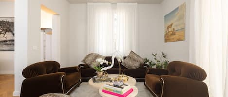 A living room with two brown sofas, a coffee table with books and decorative items, a white orchid, and a painting on the wall.