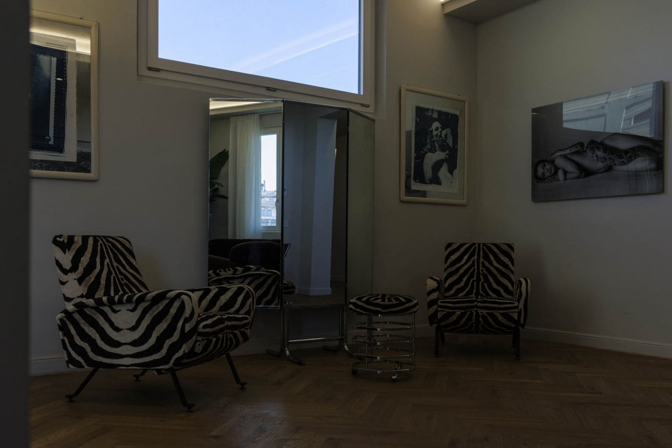 Ein geräumiges Zimmer mit großem Fenster, zebra-gestreifte Stühle, ein kleiner runder Tisch und zwei gerahmte Kunstwerke an den Wänden.