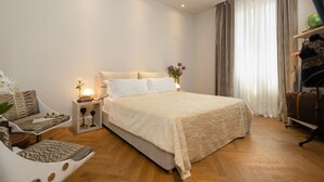 Un dormitorio con una cama grande, un sofá, una mesita de noche con lámpara y una ventana con cortinas.