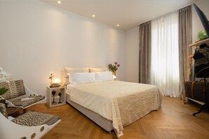 Un dormitorio con una cama grande, un sofá, una mesita de noche con lámpara y una ventana con cortinas.