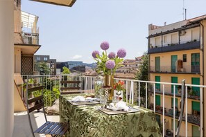 Un balcón con una mesa dispuesta para comer, un jarrón con flores y vistas a la ciudad.