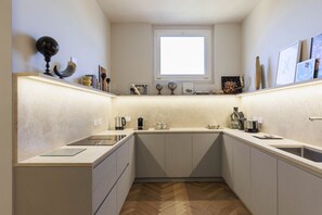 A compact kitchen with a herringbone floor pattern, a window above the sink, and various kitchen appliances and decor items on the countertops.