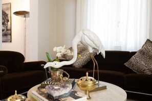 A living room with a round coffee table, a white bird sculpture, a potted plant, and decorative items.