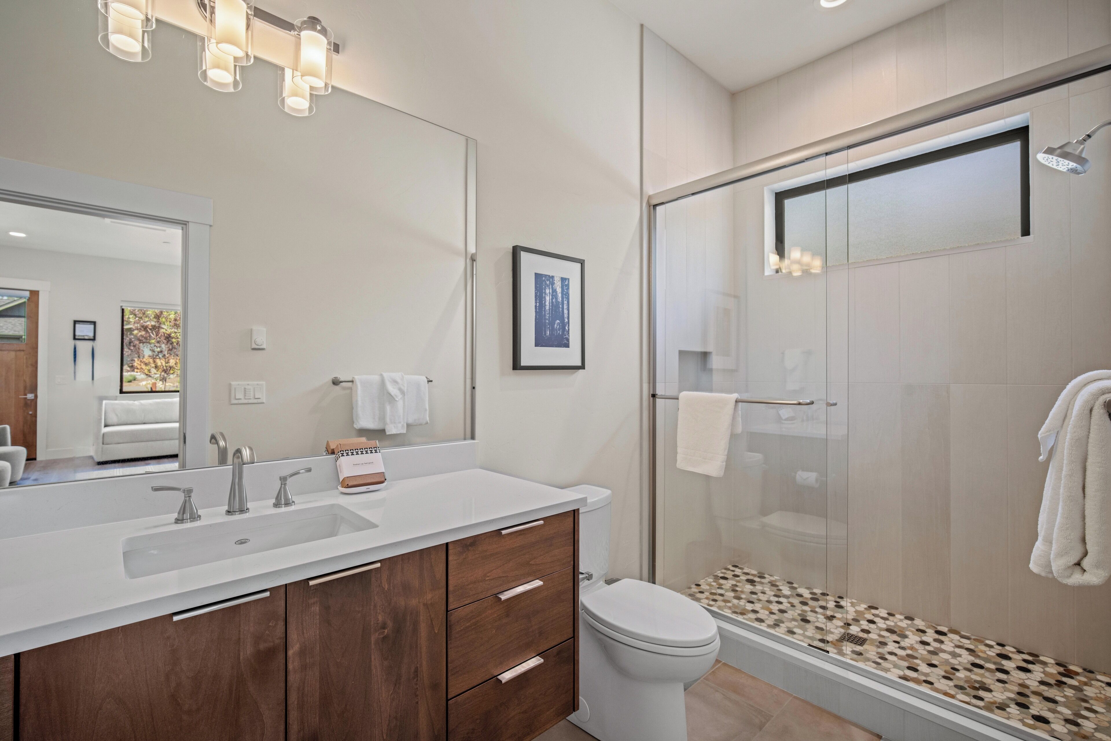 A modern bathroom with a large mirror, a white sink, a toilet, and a glass-enclosed shower area.