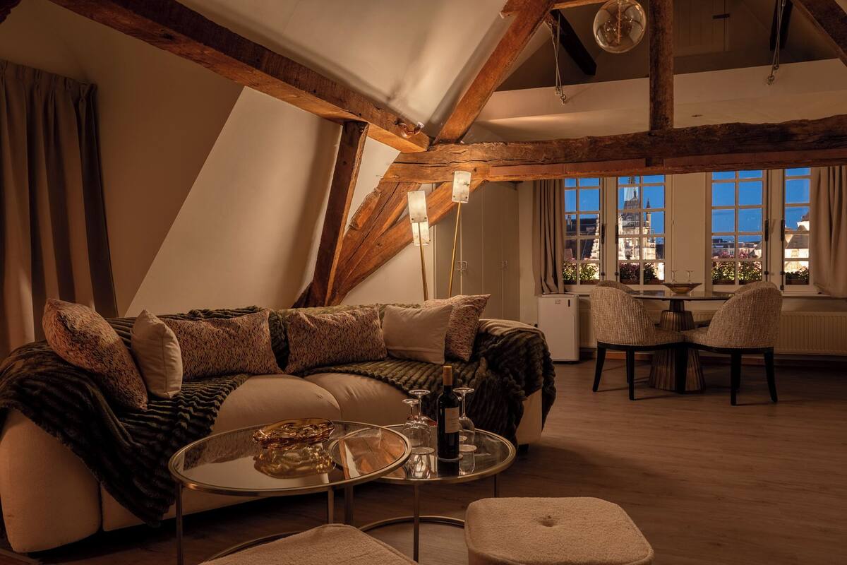 A cozy living room with a sofa, a glass coffee table, and a view of the city through large windows.