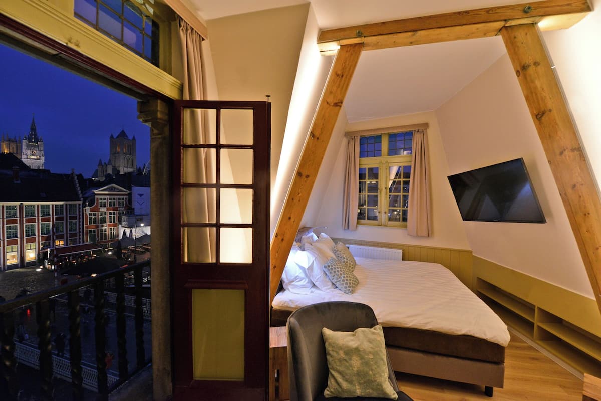 A bedroom with a bed, a chair, a TV, and a window with curtains.