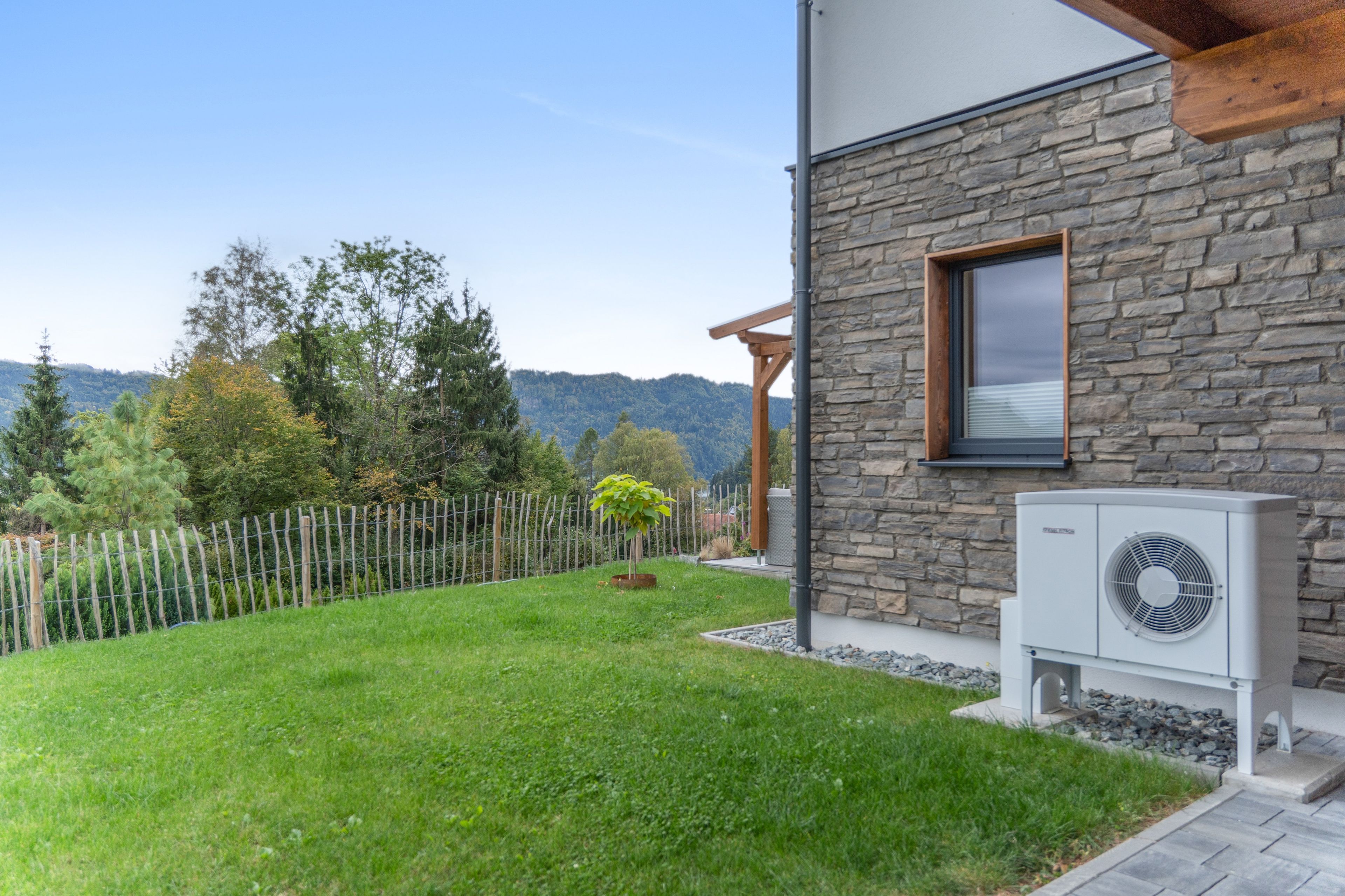 A modern house with a stone facade, a wooden deck, and a well-maintained lawn.