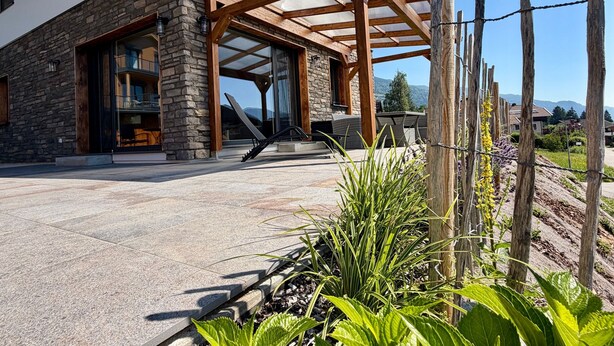 A modern house with a stone facade, a wooden pergola, and a garden with plants and flowers. - Holiday Home 'Steinrose' with Lake View, Private Terrace and Wi-Fi (Bodensdorf)