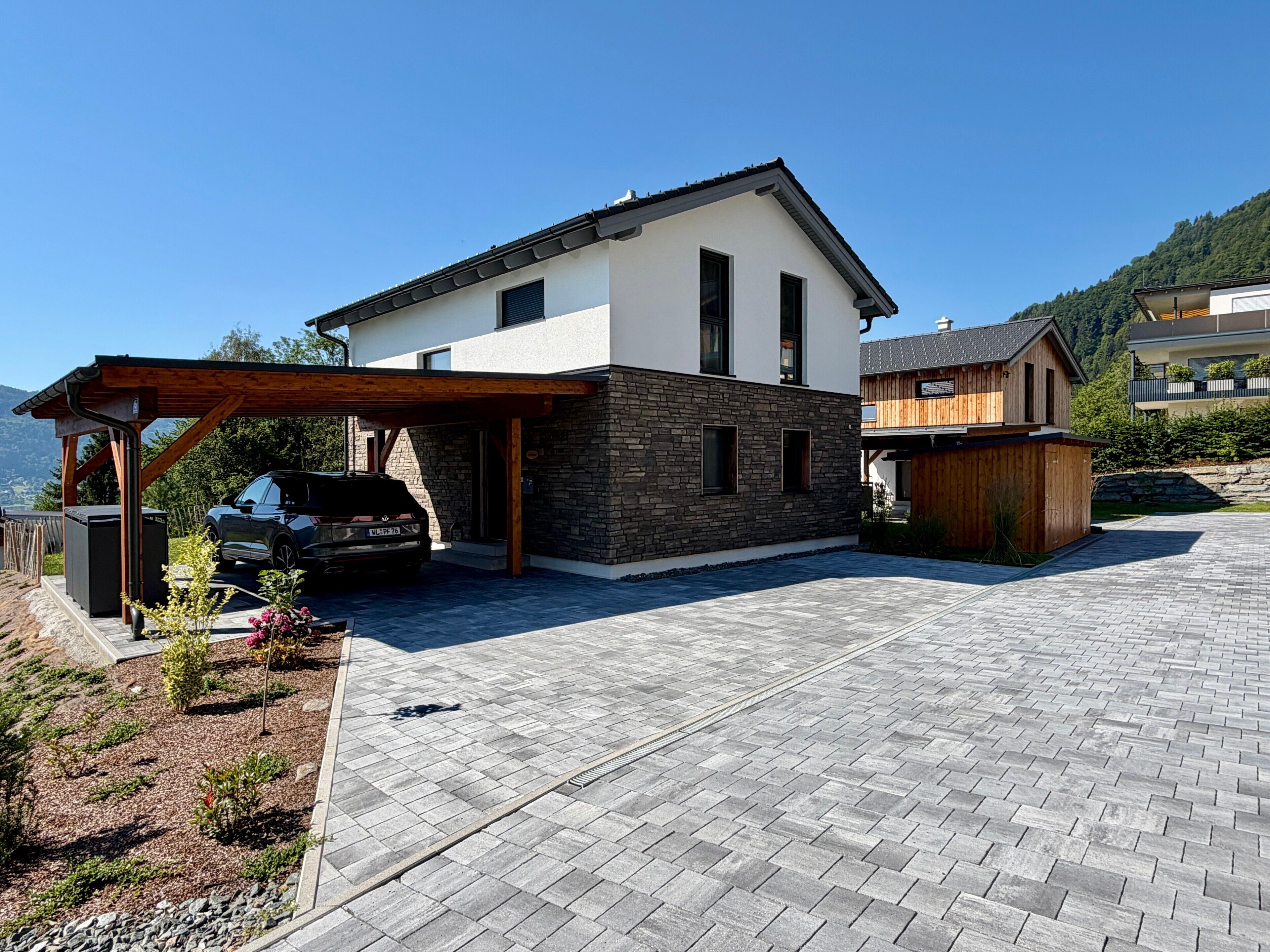 Une maison moderne à deux étages, dotée d’un abri-voiture couvert, d’une façade en pierre et d’une allée pavée.