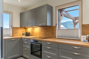 A modern kitchen with grey cabinets, a built-in oven, and a large window offering a view of the outdoors.