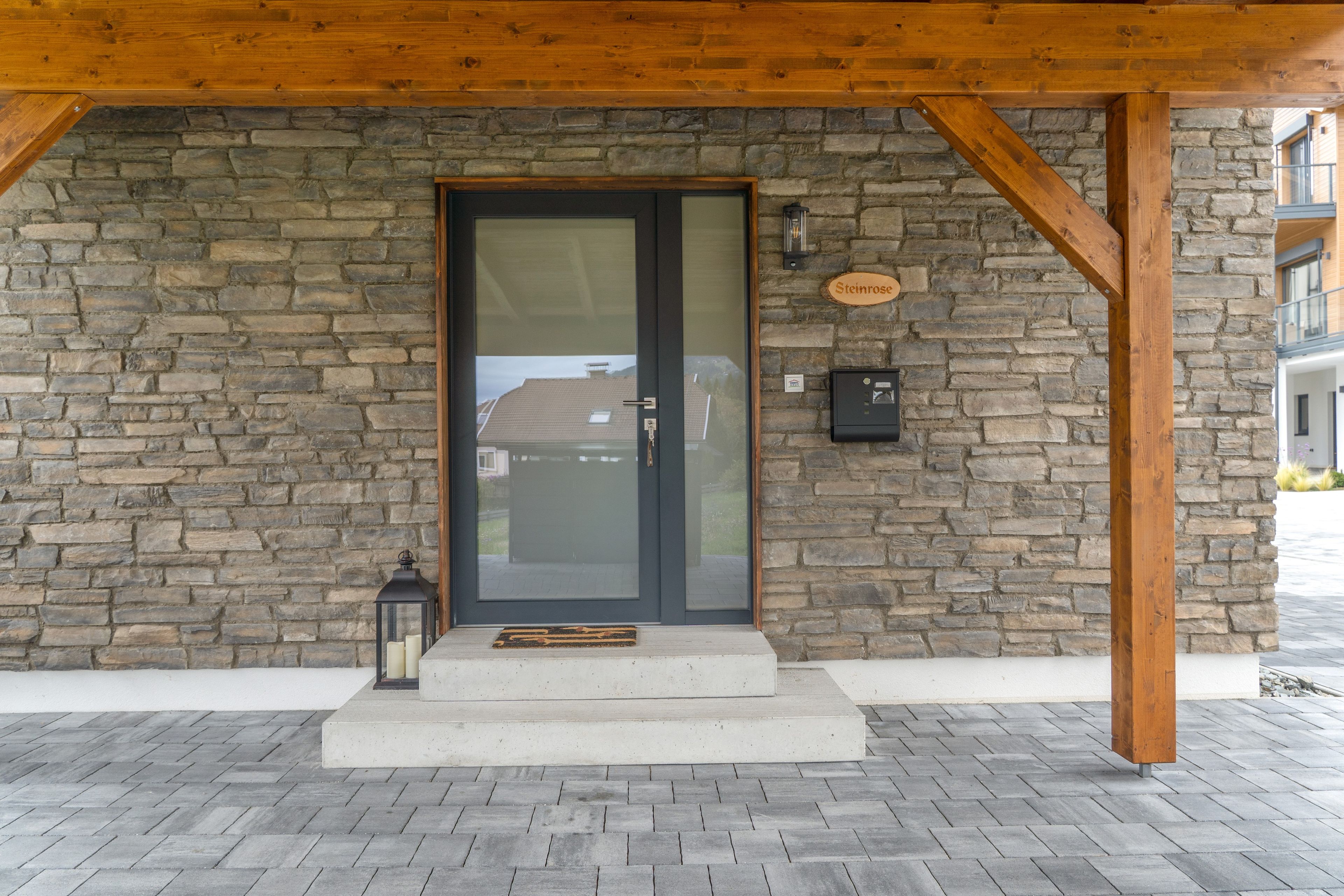 A stone facade with a wooden overhang, a glass door, and a nameplate reading 'Steinrose.'