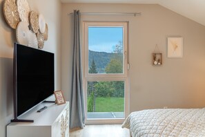 Et soveværelse med TV, et vindue med udsigt over et grønt landskab og en seng med blomstret dyne.