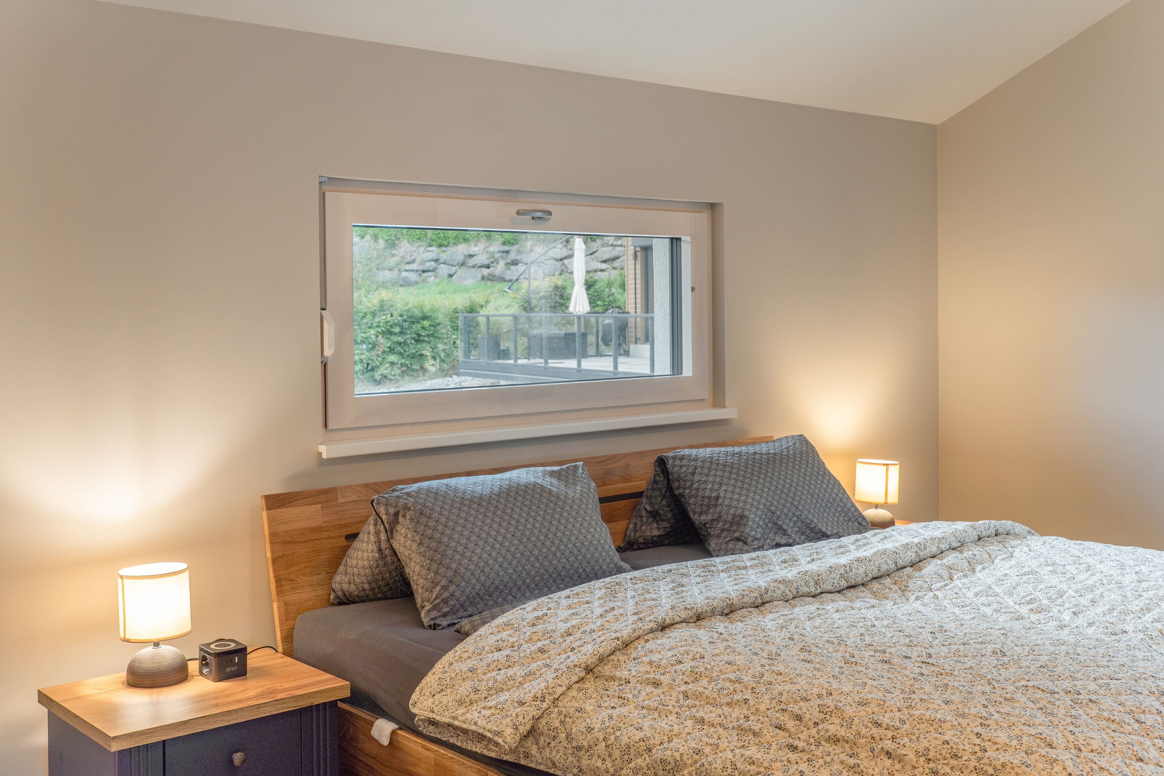A bedroom with a bed, two bedside lamps, a nightstand, and a window with a view of the outdoors.