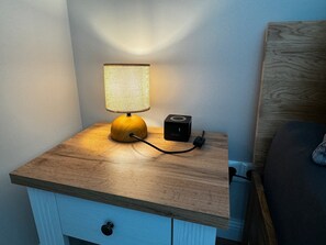 Ein Nachttisch mit Lampe, Steckleiste und kleinem Lautsprecher.