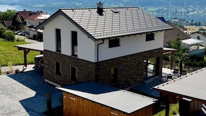 A modern house with a sloped roof, a stone facade, and a view of a lake and mountains in the background. - Holiday Home 'Steinrose' with Lake View, Private Terrace and Wi-Fi (Bodensdorf)