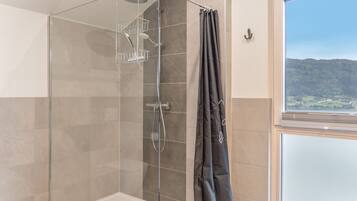 Eine gläserne Dusche mit Duschkopf, Handbrause und einer Glastrennwand für Duschutensilien.