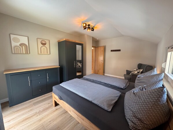 A bedroom with two beds, a wardrobe, a dresser, and a ceiling light fixture.