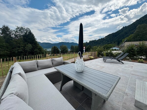 Un área de estar al aire libre con sofá, mesa y sillas, con vista a un paisaje montañoso.