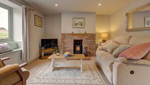 A cozy living room with a fireplace, a sofa, a coffee table, and a television. - Forget Me Not Cottage (Binham)