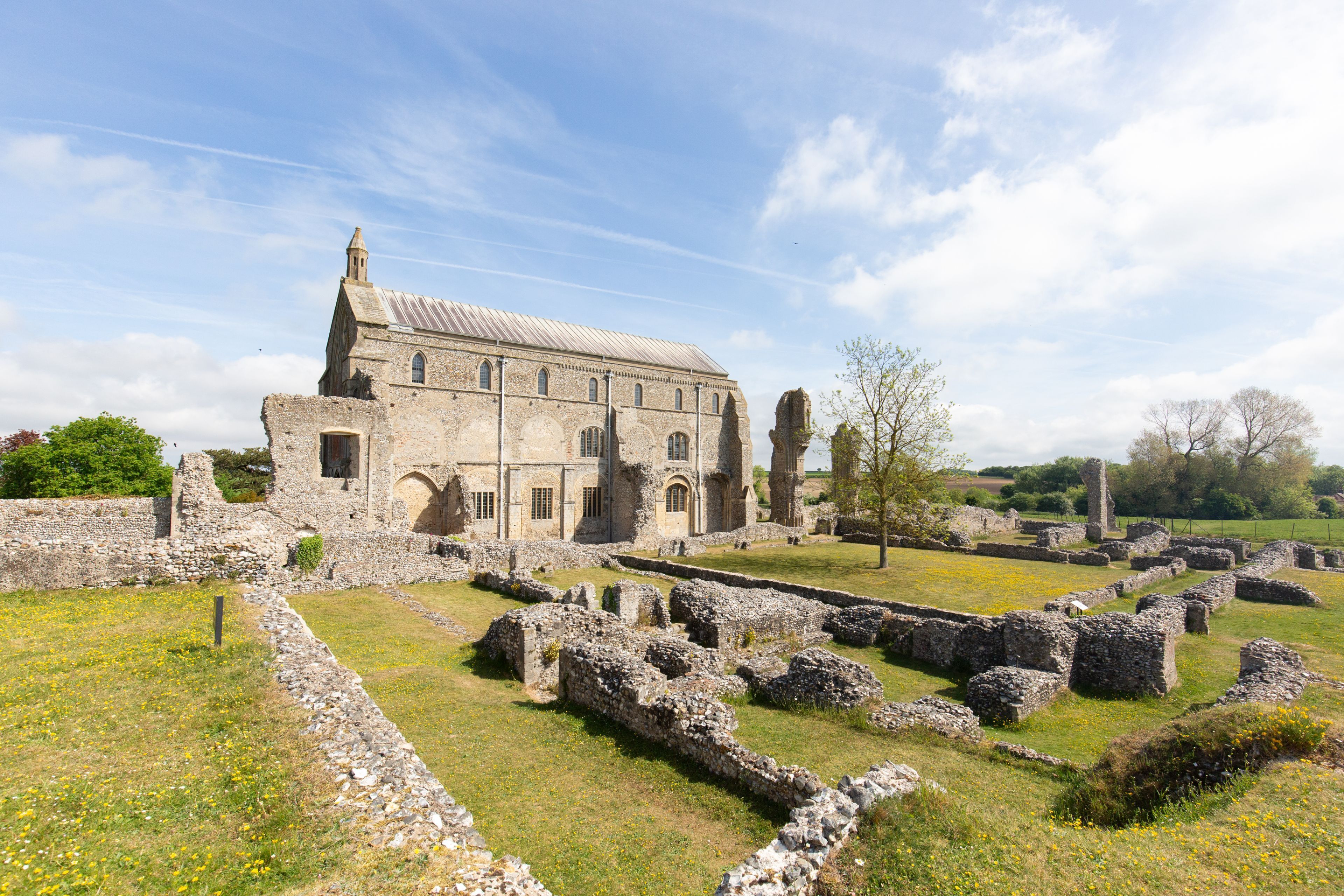 An ancient stone building with ruins in the foreground and a large, intact structure in the background.
