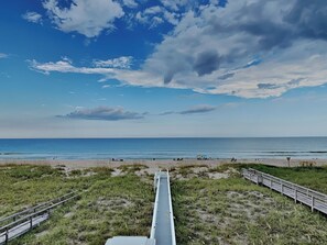 A beach with a wooden walkway leading to the water, grassy areas, and a clear sky.