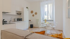 A modern, well-lit living room with a beige sofa, a coffee table, and a dining area with white chairs and a small table.