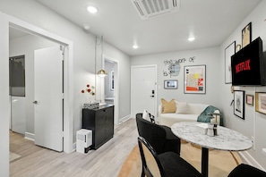 A modern living room with a sofa, a dining table, and a TV mounted on the wall.