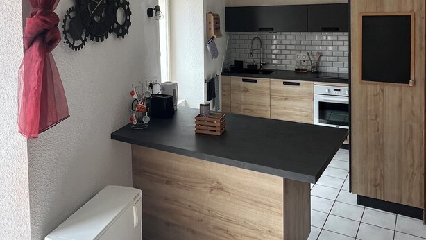 Une cuisine moderne dotée d’un îlot central, de meubles en bois, d’un four encastré et d’un plan de travail noir.