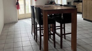Un coin repas avec une table et des chaises en bois, une cuisine en arrière-plan et une fenêtre avec des rideaux.
