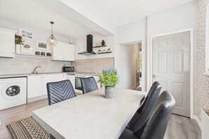 Une cuisine moderne avec des meubles blancs, un four encastré et un coin repas comprenant une table et des chaises.