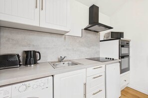 Una cocina moderna con armarios blancos, un lavamanos de acero inoxidable, un microondas y un horno.