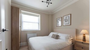 A bedroom with a bed, bedside table, wall art, and a window.