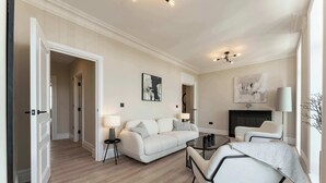 A spacious living room with a sofa, a coffee table, and a chair. There is a fireplace and artwork on the walls. - Host & Stay | Albion Place (Ramsgate)