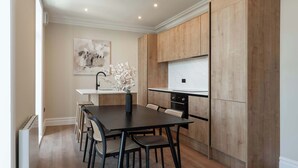 A modern kitchen with a wooden cabinet, a dining table with chairs, and a vase with flowers. - Host & Stay | Albion Place (Ramsgate)