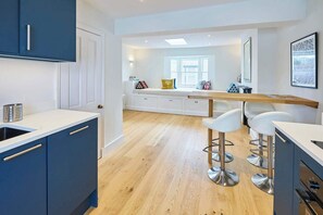 A modern kitchen with blue cabinets, a wooden dining table, and white bar stools.