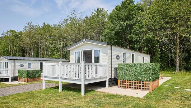 A mobile home with a deck, surrounded by greenery and trees.