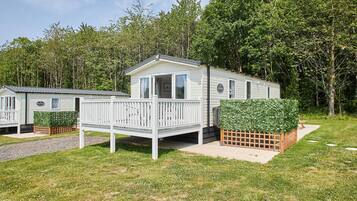 Une maison mobile dotée d’une terrasse, entourée de verdure et d’arbres.