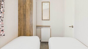 A small, neatly arranged room with two beds, a wooden accent wall, a radiator, and a mirror.