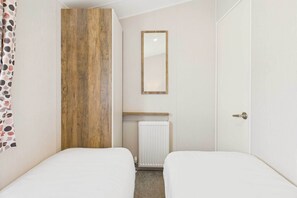 Pieni, siististi järjestetty huone, jossa on kaksi sänkyä, puinen tehosteseinä, patteri ja peili.