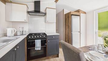 Une cuisine compacte équipée d’une cuisinière, d’un four et de meubles blancs. On y trouve une table à manger avec des assiettes et des verres.