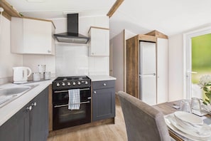 A compact kitchen with a stove, oven, and white cabinets. There is a dining table with plates and glasses.