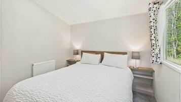 Une chambre à coucher avec un grand lit, deux tables de chevet avec des lampes, une fenêtre avec un rideau et un radiateur.