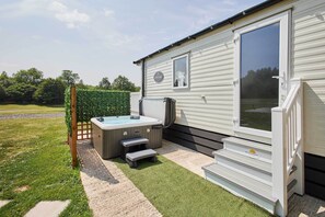 Een stacaravan met een jacuzzi, een terras en een kleine trap naar de ingang.