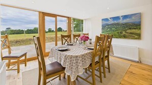 A dining area with a table set for six, large windows, and a painting of a landscape. - Host & Stay | Merrow Cottage (Great Malvern)
