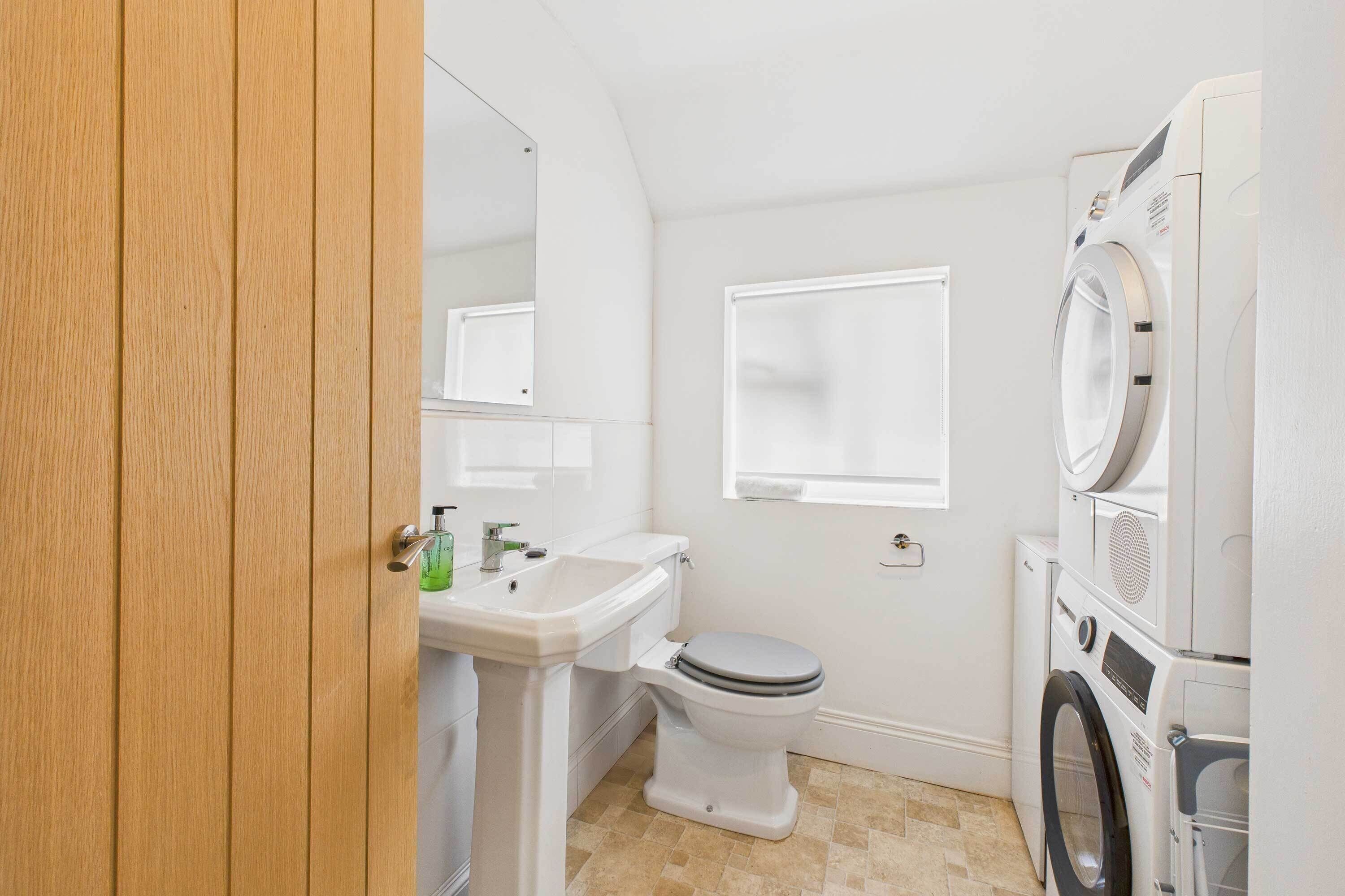 A compact bathroom with a toilet, sink, and stacked washer and dryer.