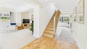 A spacious living area with a wooden staircase, a television, and a view of the outdoors. - Host & Stay | Merrow Cottage (Great Malvern)